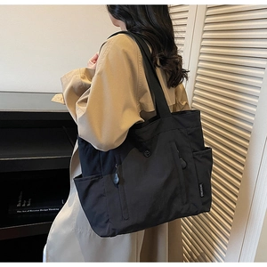 Detail of black nylon tote bag with functional zipper pockets and side slip compartment