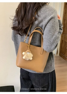 Back view of model wearing a brown lychee leather bucket bag with a cute plush pendant