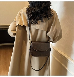 Dark brown faux leather crossbody bag worn over a khaki trench coat by a model