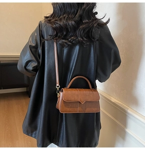 Borsa a tracolla in pelle marrone con patta a V indossata su un cappotto nero lungo