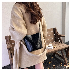 Close-up of a black glossy leather bucket bag with an adjustable shoulder strap