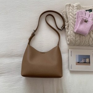 Detail of brown lychee texture bucket bag with adjustable strap on soft bedding
