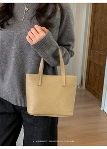 Close-up of beige lychee-patterned bucket bag held by a model in a minimalist indoor setting
