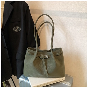 Olive green suede tote bag with buckled straps placed on a suitcase and books