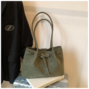 Detail of a green suede tote bag showing its slender handles and minimalist buckle design