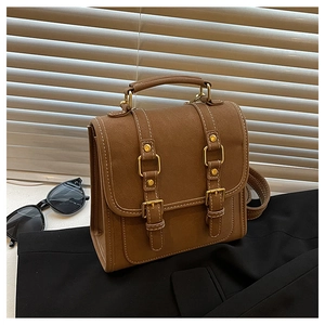 Retro brown faux leather satchel bag with buckle straps against a window blind