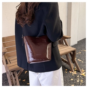 Detailed view of dark brown glossy leather bucket bag with embossed logo on the side