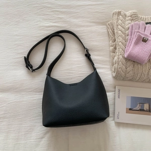 Flat lay of black lychee grain leather bucket bag with silver buckle on beige bedding