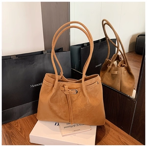 Detail of caramel suede tote bag with fine handles and drawstring closure on wood surface