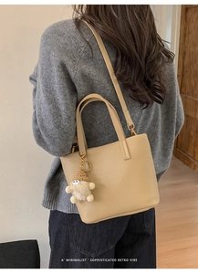 Detail of beige litchi grain leather bucket bag with soft plush dwarf charm and long strap