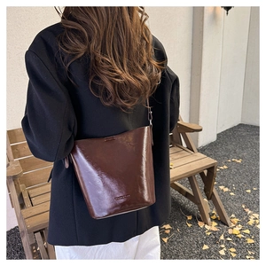Detail of dark brown glossy bucket bag with minimalist embossed logo on premium leather