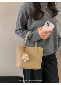 Detail of beige lychee grain leather bucket bag with a cute plush doll charm