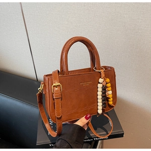 Detail of dark brown croc-embossed handbag with gold hardware and beaded charm