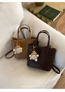 Detail of lychee pattern leather bucket bag with furry charm on a white sofa
