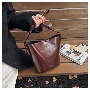 Detail of a vintage dark brown glossy bucket bag on a wooden bench with autumn leaves