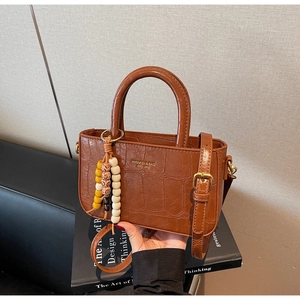 Detail of brown crocodile pattern handbag with elegant beaded pendant and slim strap