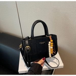 Close-up of black crocodile pattern leather handbag with gold logo and bead charm