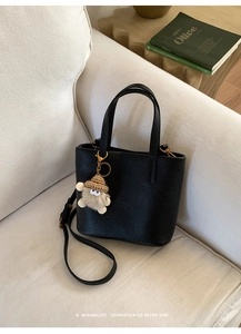 Close-up of black pebble leather bucket bag with a cute monster knit hat charm on a sofa