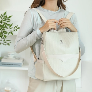 Detail of cream backpack with woven texture and rabbit logo worn by model in home setting