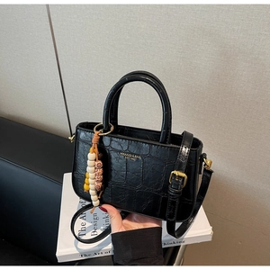Detail of black crocodile texture handbag with golden logo and bohemian bead tassel