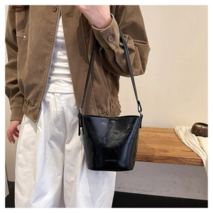 Close-up of glossy black leather bucket bag with fine texture and subtle text detail