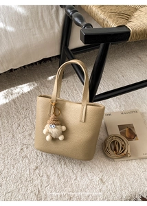 Close-up of beige leather bucket bag with plush charm and strap on a soft rug