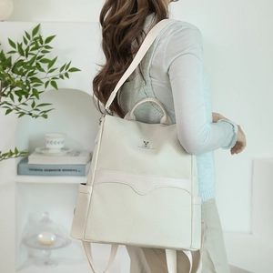 Detail view of stylish cream backpack with woven texture and logo shown on model