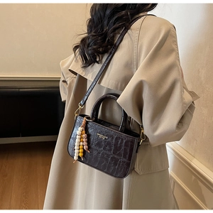 Detail of dark brown croc-effect handbag with gold logo and vintage beaded charm