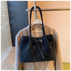 Close-up of black suede tote bag with strap buckle detail and thin shoulder straps