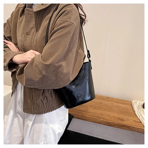 Glossy black bucket bag shown with vintage brown jacket on model for office wear