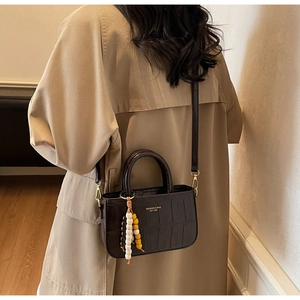 Detail of dark brown crocodile pattern bag with wooden bead charm and long shoulder strap