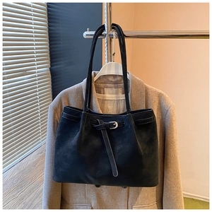 Detail of a black suede tote bag with slim buckles hanging on a beige coat
