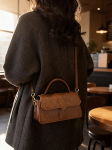 Borsa a tracolla vintage marrone in ecopelle con dettagli dorati indossata su un cappotto