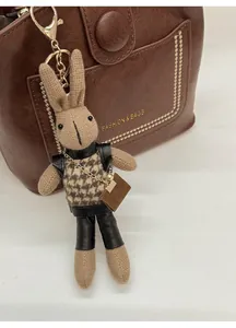 Detail of a rabbit charm in knitted khaki fabric with houndstooth vest and metal clasp