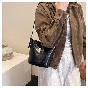 Detail of the high-gloss black leather texture and embossed logo on the bucket bag
