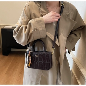Detail of dark brown faux crocodile leather handbag with wooden bead charm on a beige coat