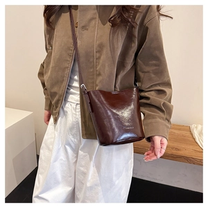 Detail of vintage brown leather bucket bag with debossed logo on model with chic outfit