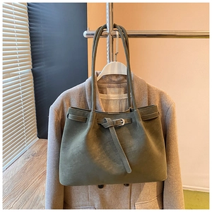 Detail of green suede tote bag with slim handles and metal buckle on wool coat background