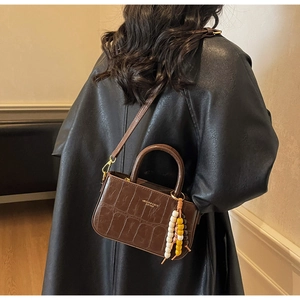 Detail of dark brown crocodile embossed crossbody bag with boho bead tassel ornament