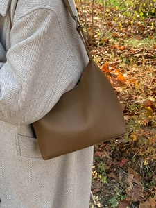 Minimalist caramel brown pebble leather bucket shoulder bag shown on a grey wool coat