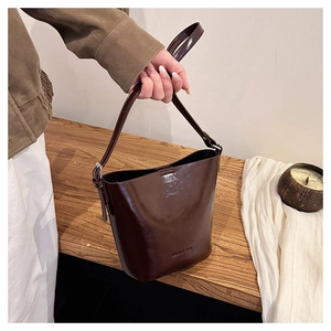Detail of dark brown polished leather bucket bag with embossed text and silver metal hardware