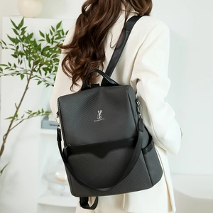 Detail of dark grey woven fabric backpack with silver rabbit logo on a female model
