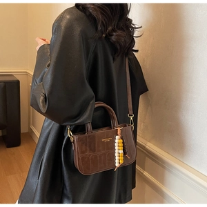 Detail of a brown croc-effect crossbody bag with bead charm and golden brand text