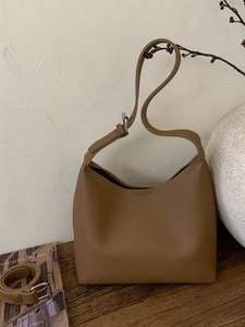 Minimalist earth-tone bucket bag with lychee leather texture and adjustable strap