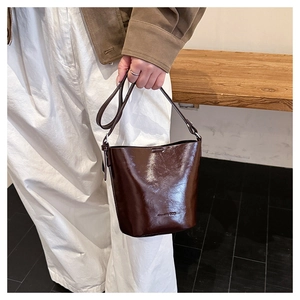 Macro view of dark brown glossy bucket bag with embossed logo and adjustable strap