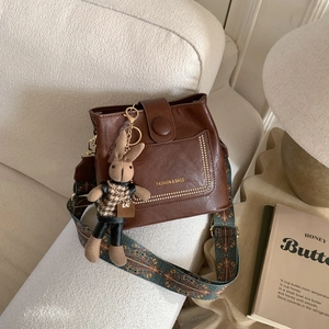 Close-up of brown leather bucket bag featuring a colorful ethnic style wide woven shoulder strap