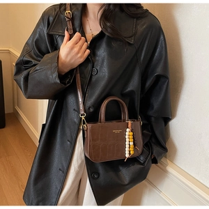 Close-up of brown crocodile texture shoulder bag with stylish beaded pendant detail