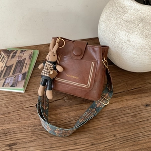 Close-up of brown bucket bag with ethnic strap, rabbit charm, and golden lettering