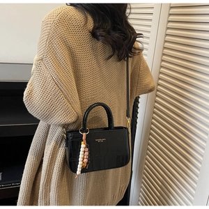 Detail of black crocodile texture handbag with gold logo and colorful beaded chain charm
