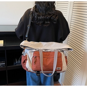 Vista posteriore di un modello con grande borsa da viaggio in tela grigia e arancione a tracolla